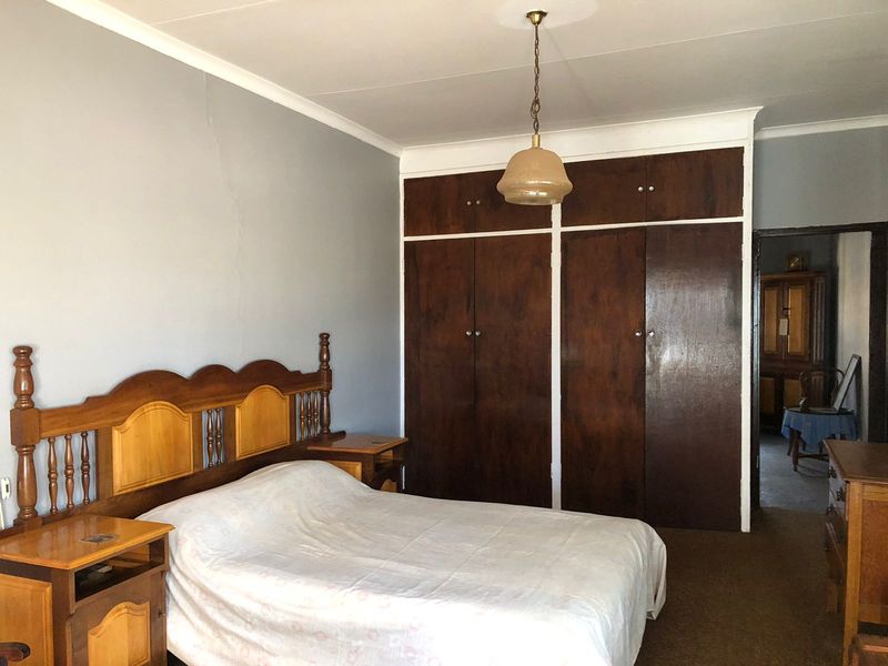 A bedroom featuring built-in wooden cupboards, a ceiling pendant light, and coving, with a visible crack on the wall.