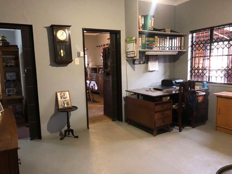 A functional home office space featuring built-in shelving, security bars on the windows, and a security gate at the entrance.