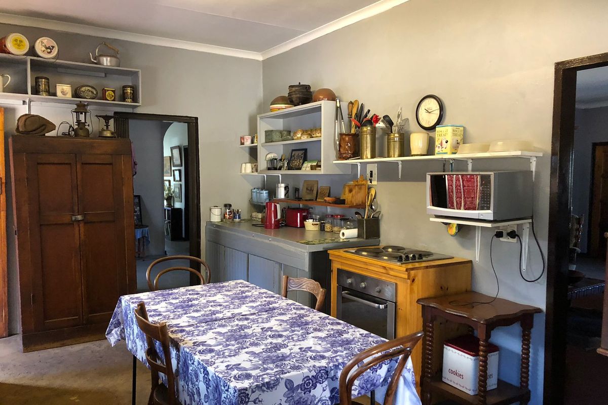 A functional kitchen area featuring built-in oven, electric hob, and open wall-mounted shelving, offering potential for modernization and improved layout.