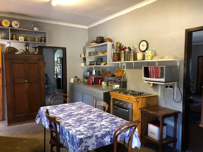 A functional kitchen area featuring built-in oven, electric hob, and open wall-mounted shelving, offering potential for modernization and improved layout.