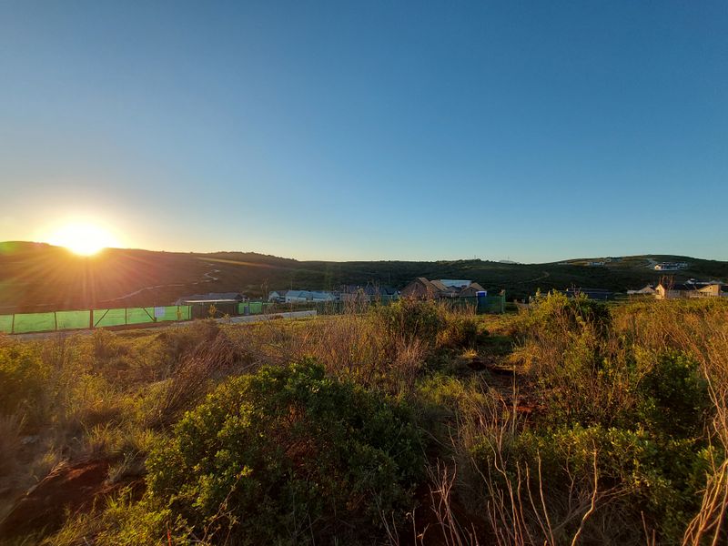 A scenic landscape view overlooking a residential area at sunset, featuring natural vegetation and distant hills.