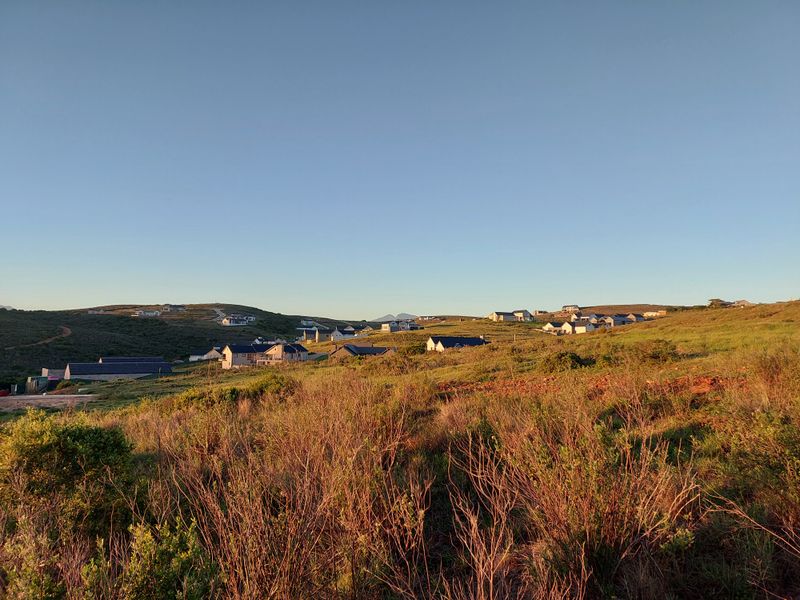 A scenic landscape view overlooking a residential estate with rolling hills and natural vegetation under a clear sky.