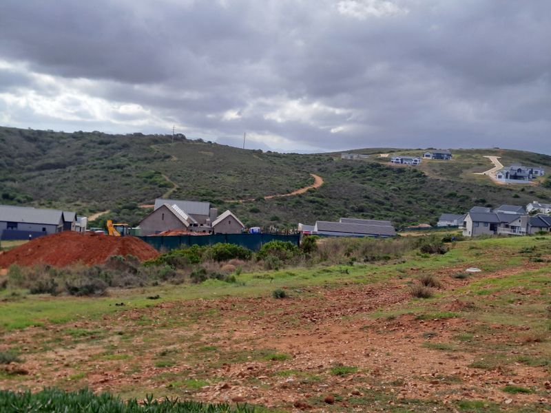 A wide-angle view of a developing residential estate set against a hilly landscape under a cloudy sky.