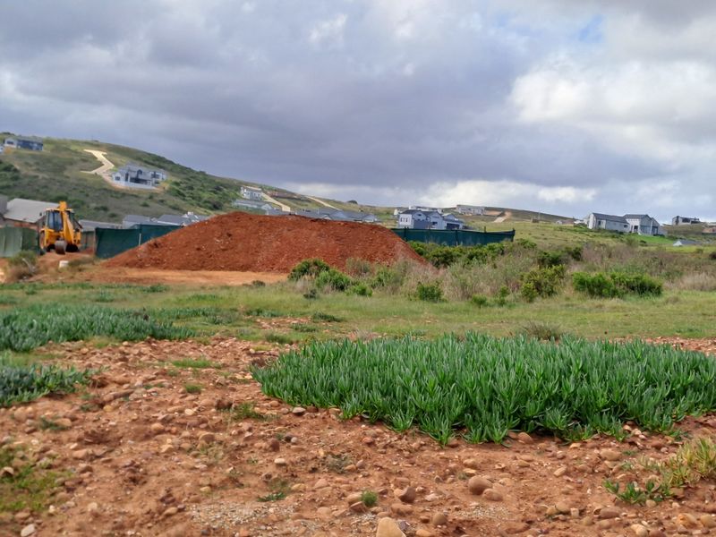 A view of an undeveloped plot of land featuring earthworks and surrounding residential development in the distance.