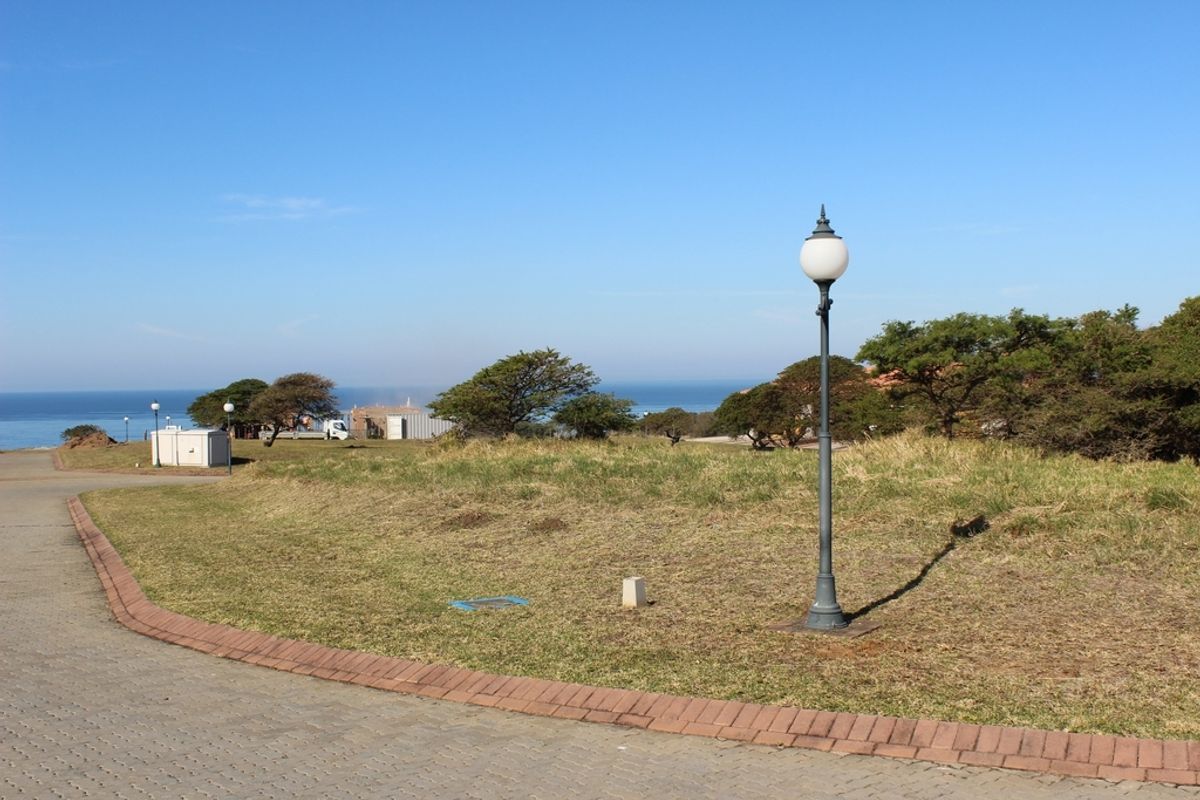 A vacant residential plot featuring paved access, established landscaping, and a street lamp, offering scenic coastal views in a quiet estate setting.