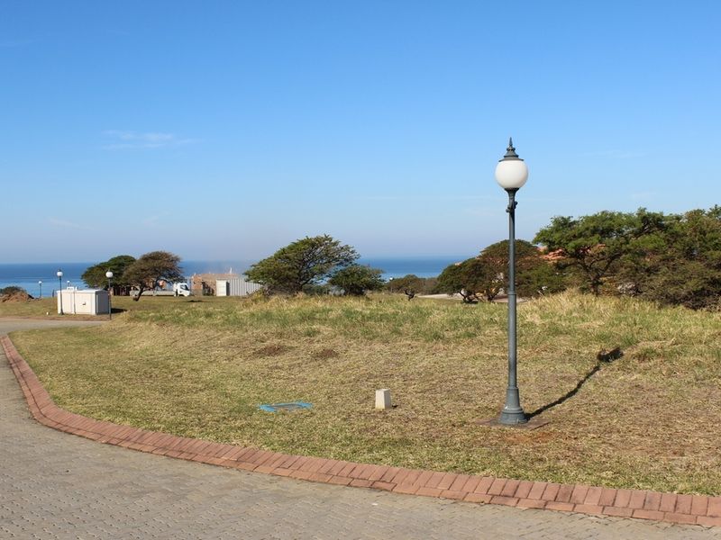 A vacant residential plot featuring paved access, established landscaping, and a street lamp, offering scenic coastal views in a quiet estate setting.
