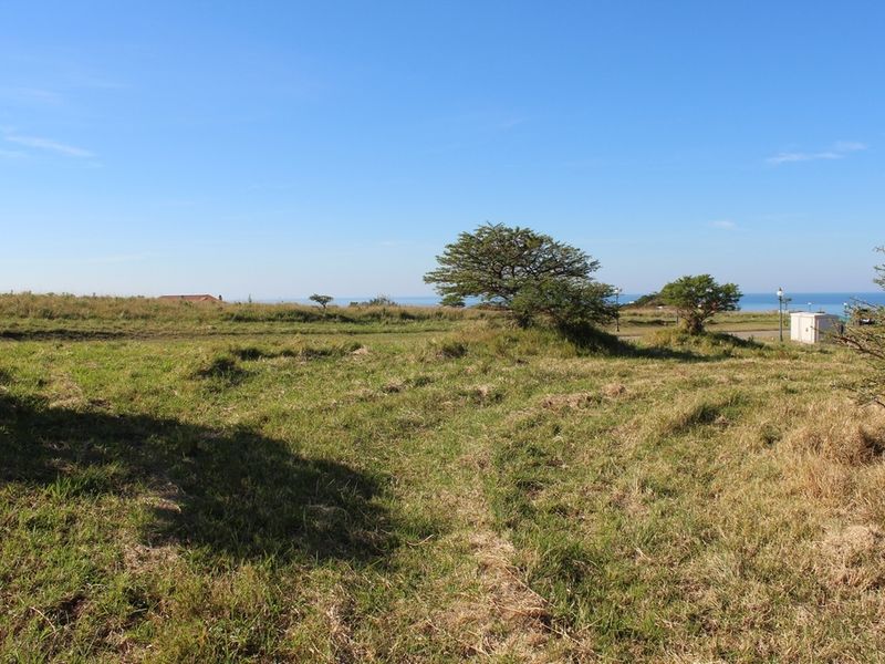 A vacant residential plot featuring natural grass terrain, scattered trees, and distant ocean views, offering a blank canvas for future development.