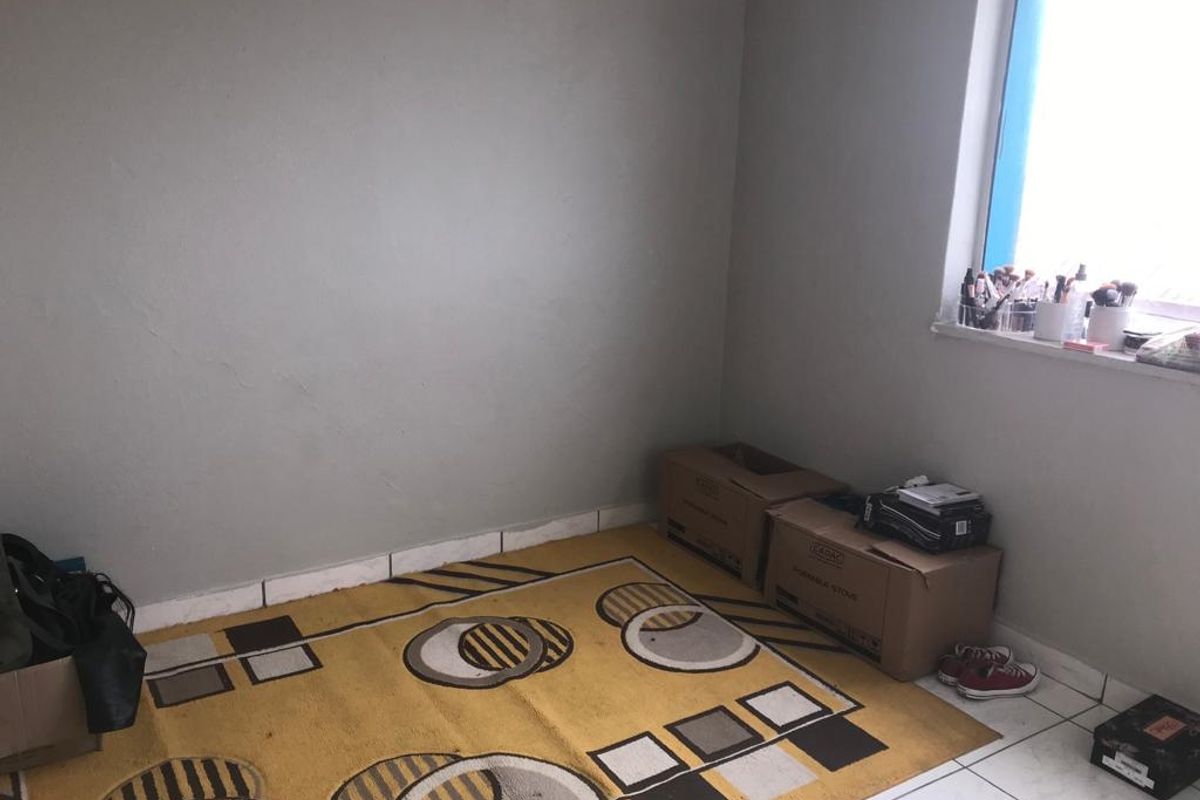 A simple bedroom space featuring tiled flooring and a window, currently used for storage.