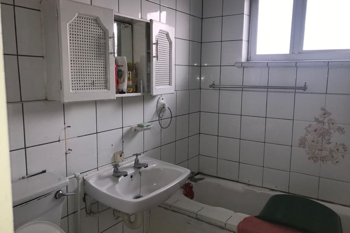 A dated bathroom featuring white wall tiles, a standard bathtub, a pedestal basin, and a wall-mounted storage cabinet.