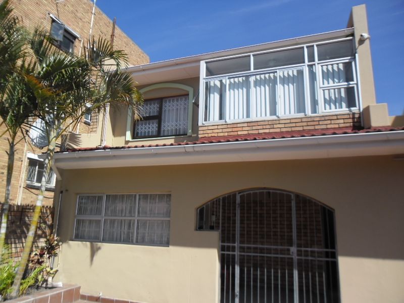 Front elevation of a townhouse featuring a secure gated entrance, brick facade, and an enclosed upper-level balcony with security bars.