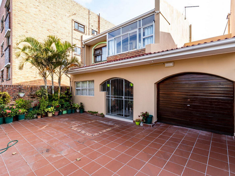 Front exterior view of the townhouse featuring a tiled driveway, secure garage access, and an enclosed upper-level balcony.