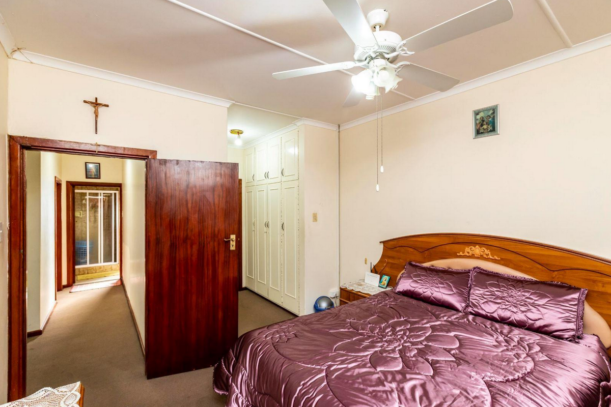 A bedroom featuring built-in cupboards, a ceiling fan, and carpeted flooring, with an adjoining hallway leading to a bathroom area.