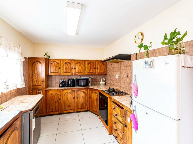 A functional kitchen featuring traditional wooden cabinetry, tiled backsplash, built-in oven, gas hob, and extractor fan with tiled flooring throughout.