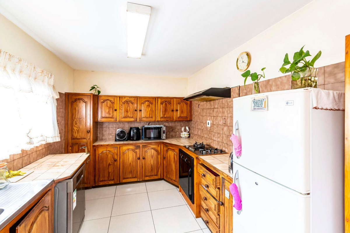 A functional kitchen featuring traditional wooden cabinetry, tiled backsplash, built-in oven, gas hob, and extractor fan with tiled flooring throughout.