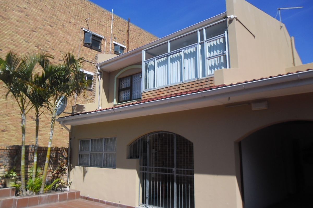 Rear exterior view of the townhouse featuring a tiled patio area, security gate, and an enclosed upper-level balcony.