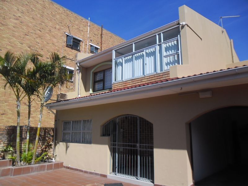 Rear exterior view of the townhouse featuring a tiled patio area, security gate, and an enclosed upper-level balcony.