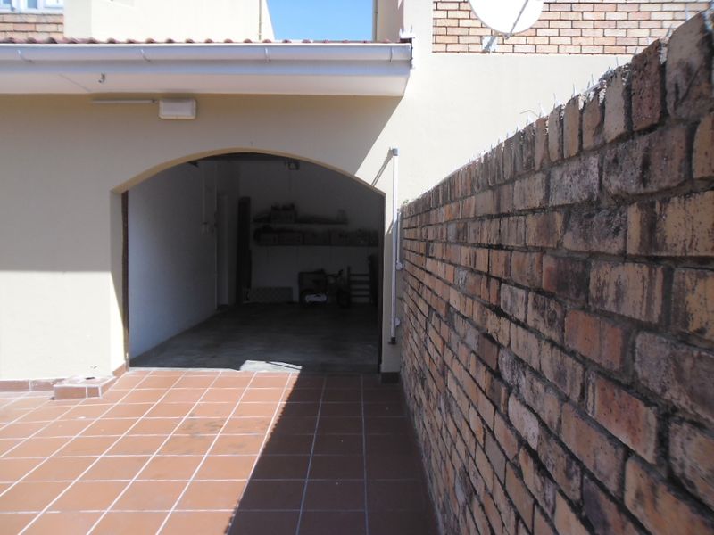 An exterior view of a townhouse garage entrance featuring a brick boundary wall and tiled patio area.
