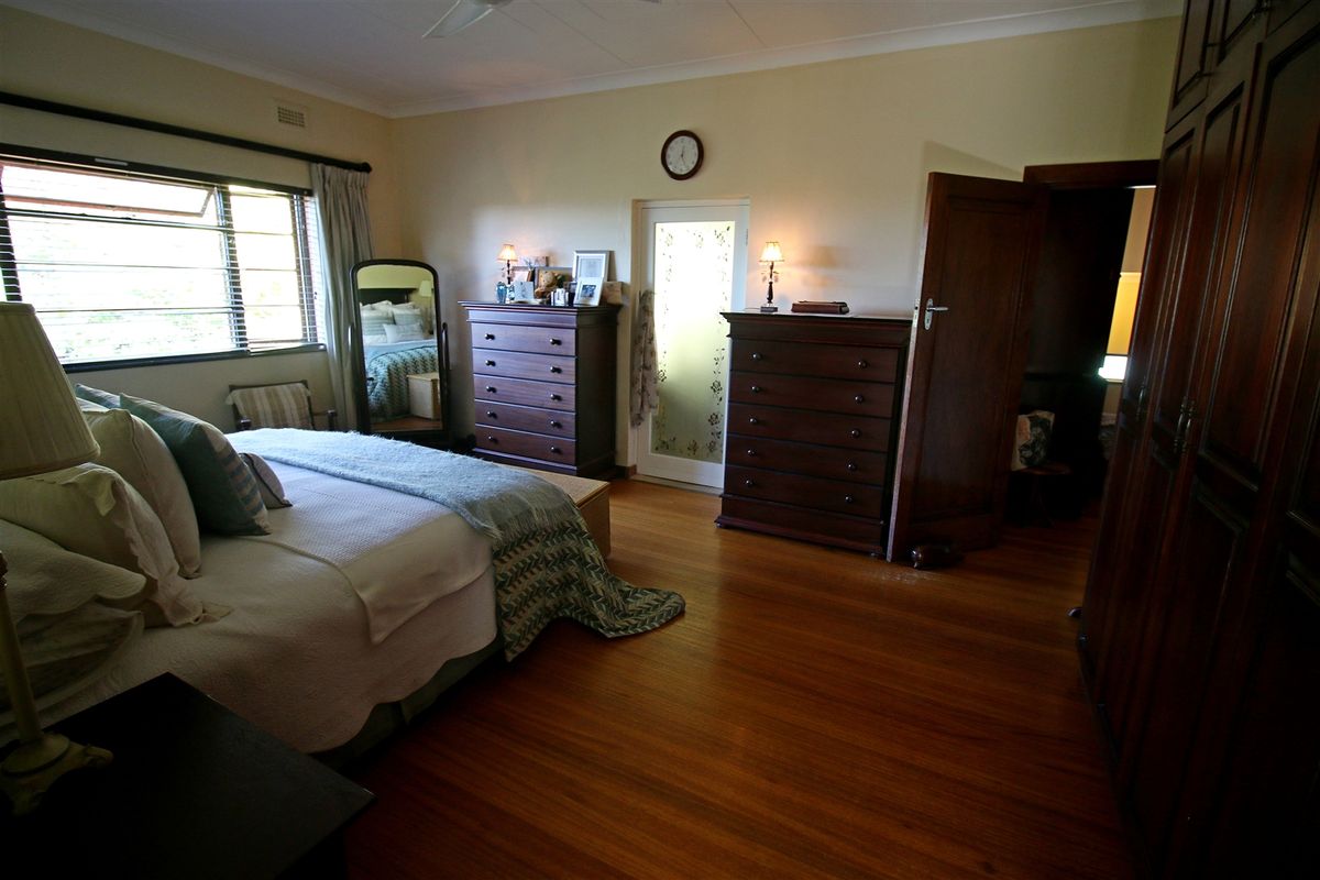 Spacious bedroom featuring polished hardwood flooring, built-in wooden cupboards, and a ceiling fan, offering a warm and traditional aesthetic.