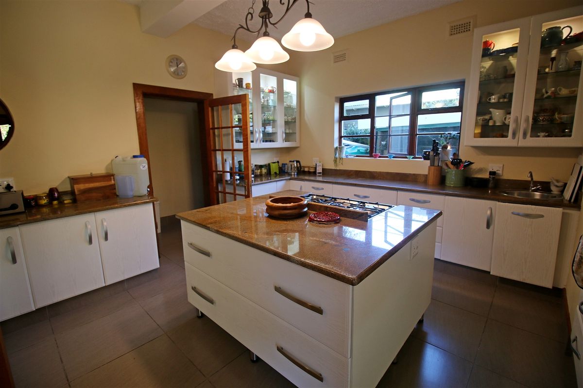 Spacious kitchen featuring a central island with a built-in gas hob, granite countertops, ample cabinetry, and tiled flooring.