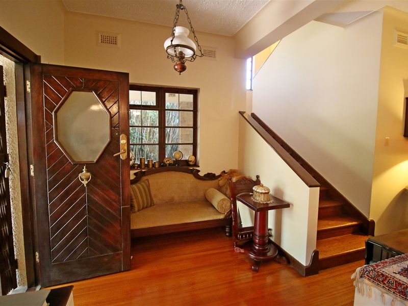 Welcoming entrance hall featuring polished timber flooring, a classic timber staircase with handrail, and a decorative solid timber front door.