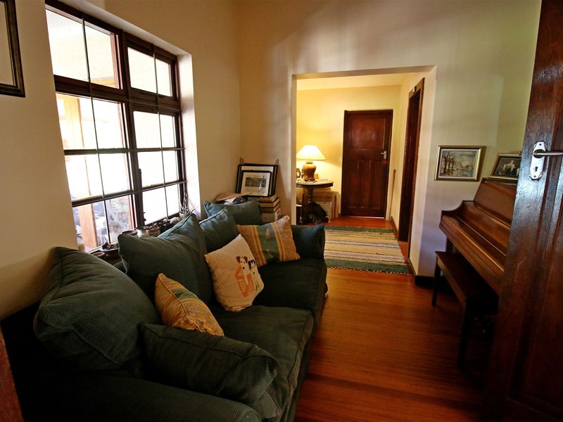 A cozy living room featuring warm timber flooring, a large multi-pane window, and classic timber door frames leading to an adjacent hallway.