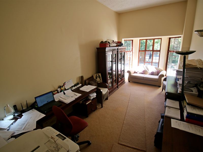 A functional home office space featuring large windows that provide natural light and carpeted flooring throughout.