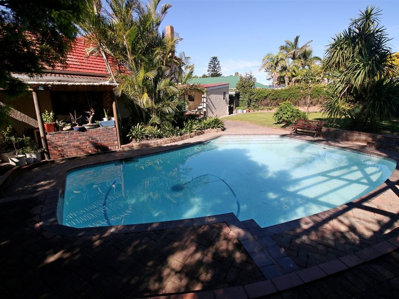 Outdoor pool area featuring a swimming pool, brick paving, and a covered patio space set within a landscaped garden.