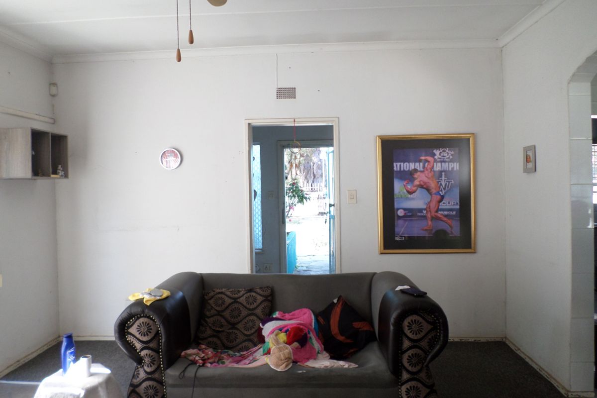A living room area featuring a ceiling fan and ventilation grille, with visible wear on the walls and carpet flooring.
