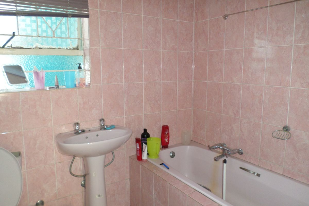 A dated bathroom featuring pink ceramic wall tiles, a pedestal basin, and a built-in bathtub with visible staining.