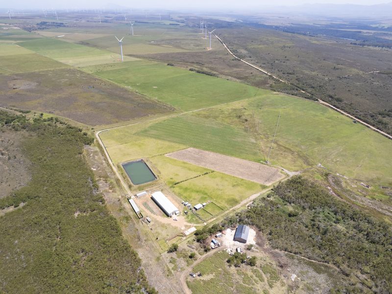 Aerial view of a large rural property featuring agricultural buildings, a water reservoir, and expansive open land with surrounding wind turbines.
