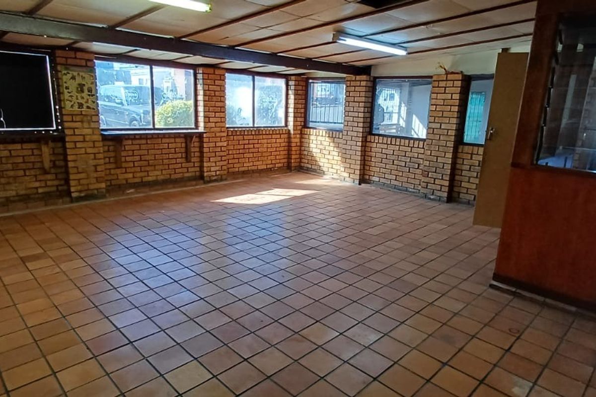 An empty office space featuring exposed brick walls, tiled flooring, and timber-framed glass partitions, offering a functional layout for a professional workspace.