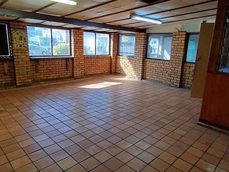 An empty office space featuring exposed brick walls, tiled flooring, and timber-framed glass partitions, offering a functional layout for a professional workspace.
