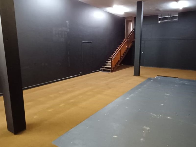 Spacious open-plan office area featuring dark painted walls, carpeted flooring, support columns, and an internal wooden staircase leading to an upper level.