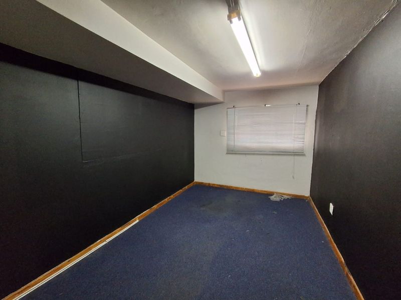 An empty office space featuring dark painted walls, blue carpeting, and functional fluorescent lighting, suitable for a professional workspace.