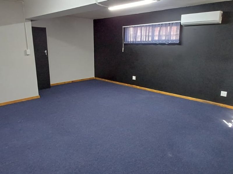 An empty office space featuring blue carpeting, a wall-mounted air conditioning unit, and a dark accent wall.
