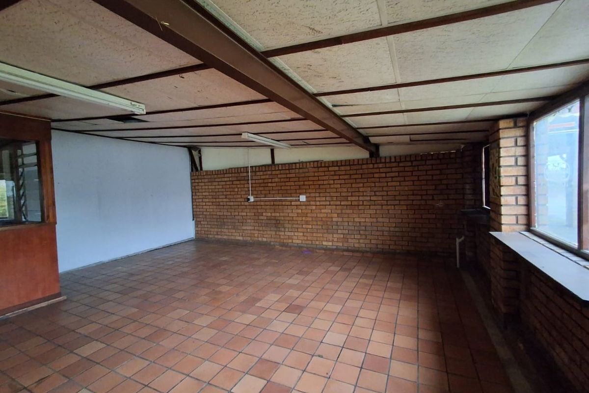 An empty office space featuring exposed brick walls, terracotta tile flooring, and an exposed steel beam ceiling structure, offering a blank canvas for renovation.