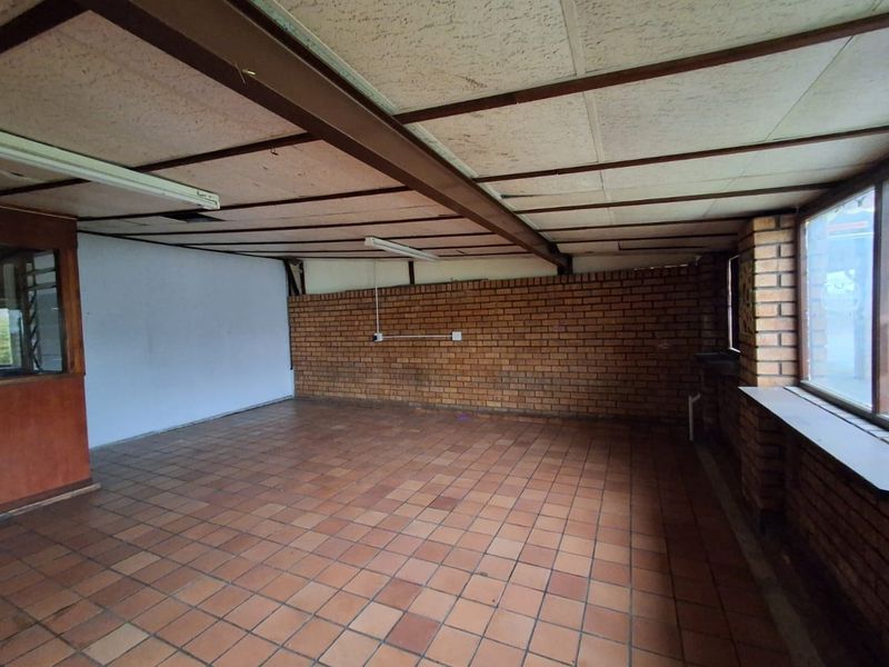 An empty office space featuring exposed brick walls, terracotta tile flooring, and an exposed steel beam ceiling structure, offering a blank canvas for renovation.