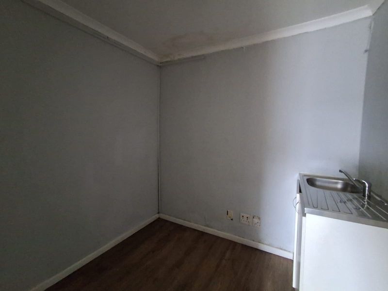 A small, empty office space featuring laminate flooring, a built-in stainless steel sink unit, and visible signs of ceiling water damage.