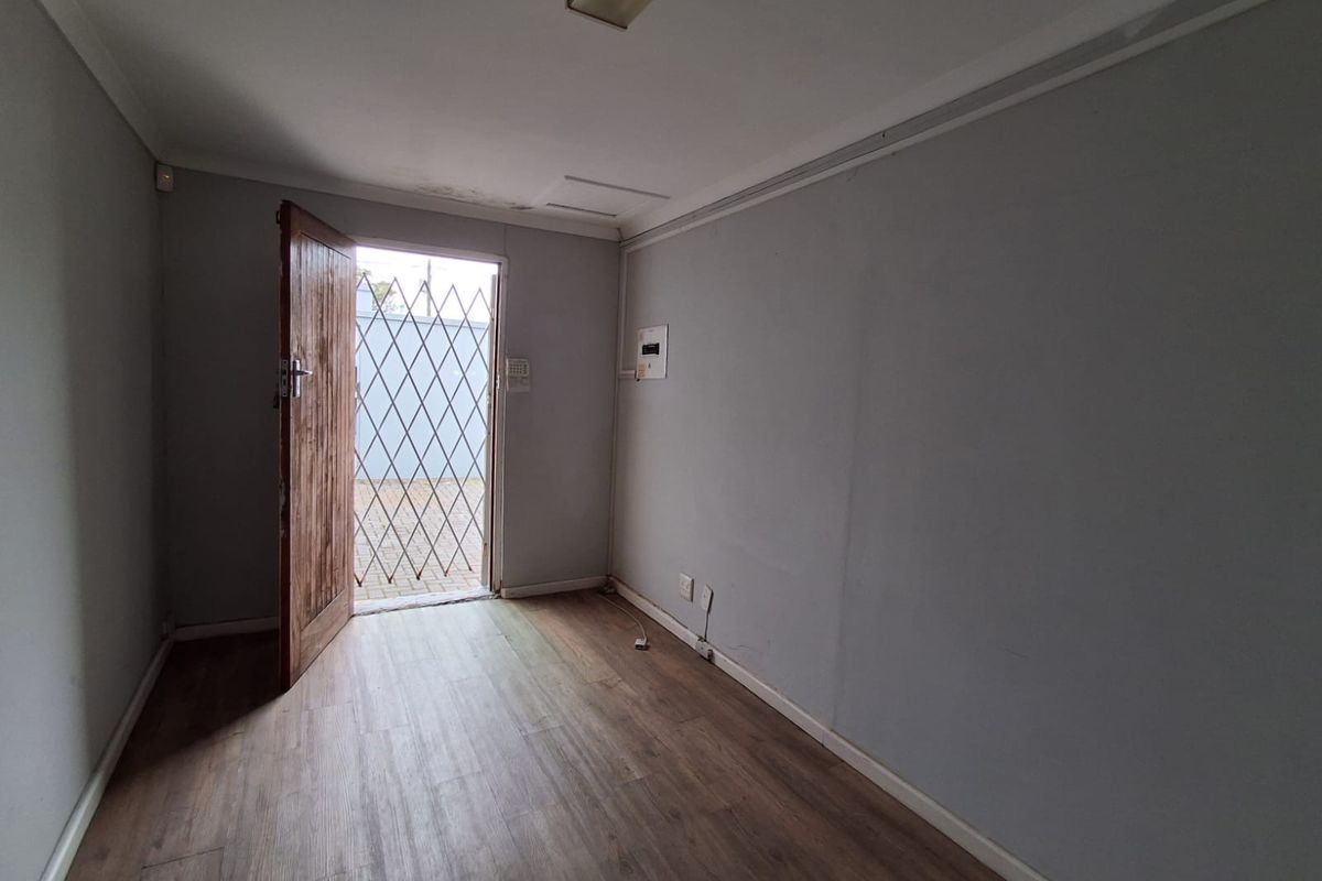 A vacant office space featuring laminate flooring, a security gate at the entrance, and integrated electrical and alarm infrastructure.