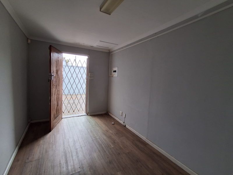 A vacant office space featuring laminate flooring, a security gate at the entrance, and integrated electrical and alarm infrastructure.