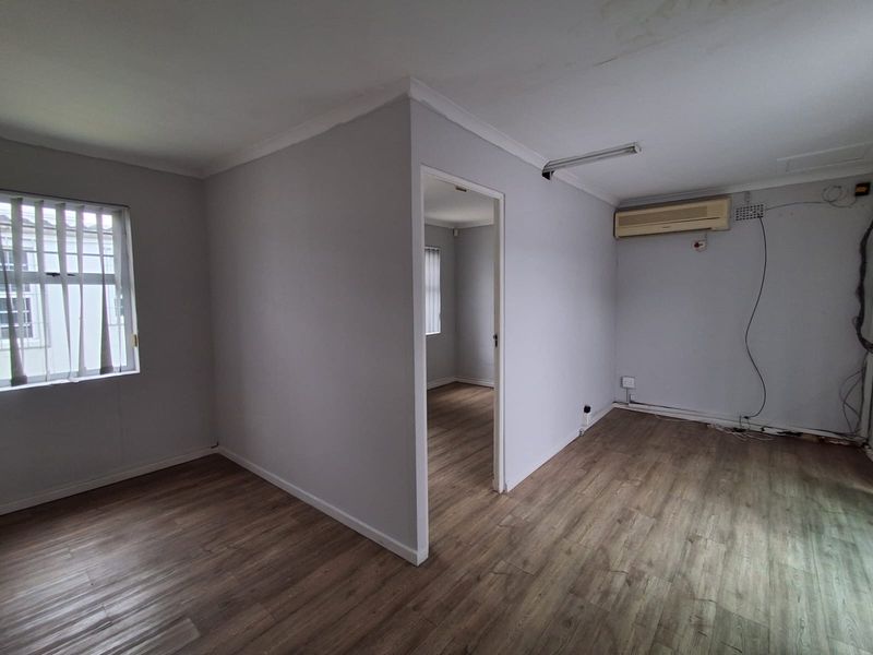 Empty office space featuring laminate flooring, an air conditioning unit, and neutral walls, offering a blank canvas for professional workspace configuration.