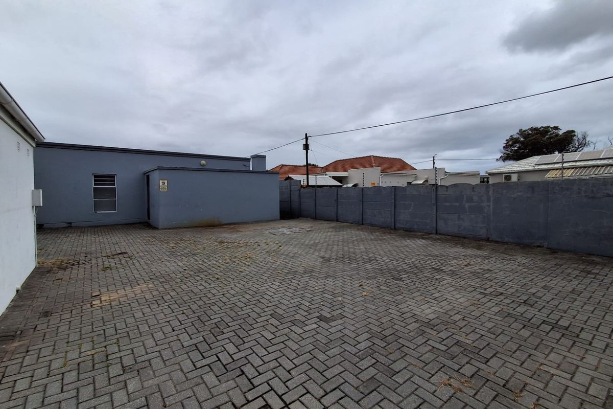 A paved rear exterior area featuring a precast concrete boundary wall and access to the main office building structure.