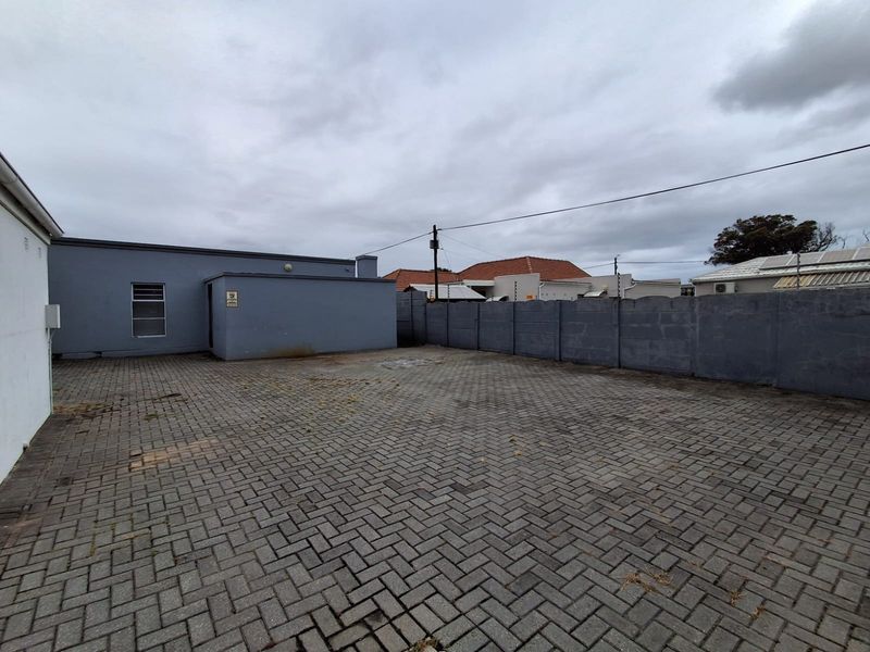 A paved rear exterior area featuring a precast concrete boundary wall and access to the main office building structure.
