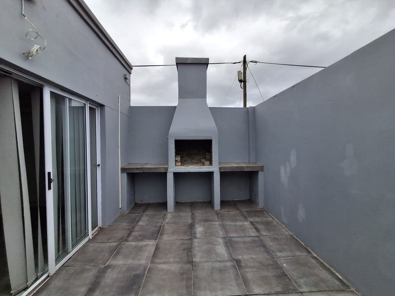 Outdoor patio area featuring a built-in braai, tiled flooring, and direct access to the interior via sliding glass doors.