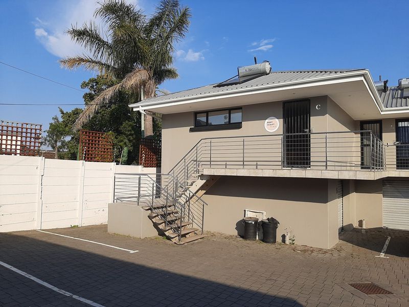 Exterior view of a commercial office unit featuring a paved parking area, external staircase with steel balustrades, and a solar water heating system.