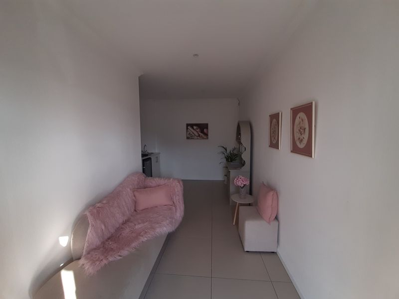 A bright office space featuring neutral tiled flooring, recessed downlighting, and a small kitchenette area in the rear.