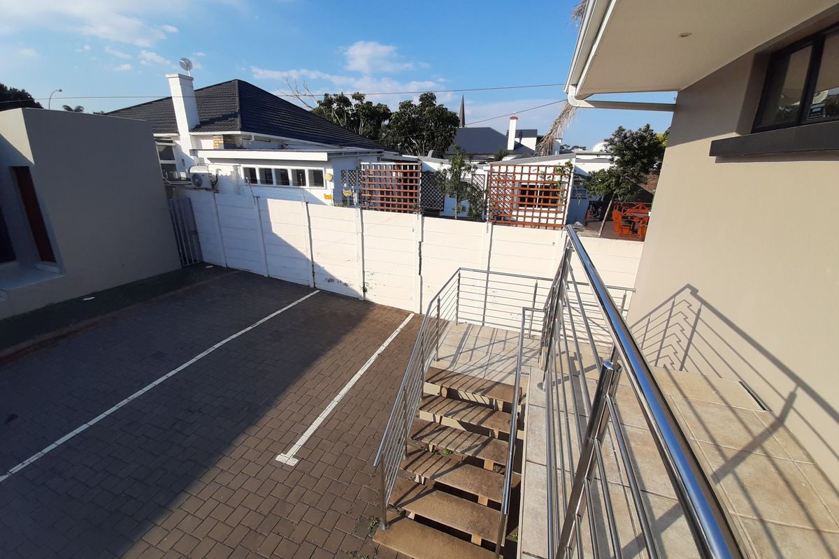 Rear exterior view showing a paved parking area, external staircase with stainless steel balustrades, and secure boundary walling.