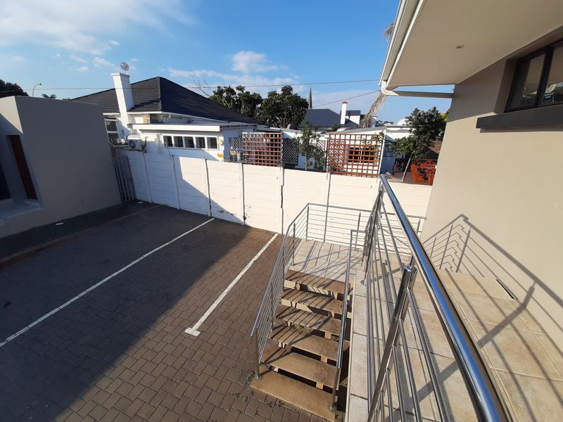 Rear exterior view showing a paved parking area, external staircase with stainless steel balustrades, and secure boundary walling.