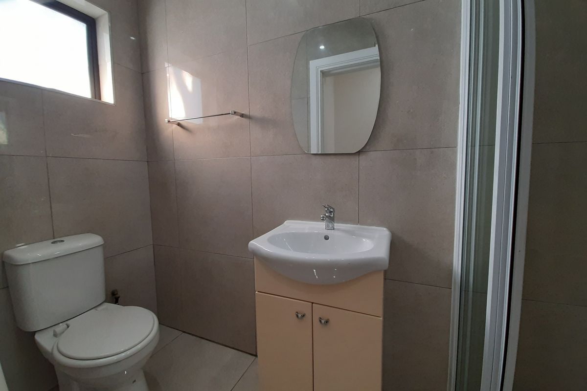 A clean, modern bathroom featuring a vanity cabinet with basin, a toilet, and a glass-enclosed shower with neutral wall and floor tiling.