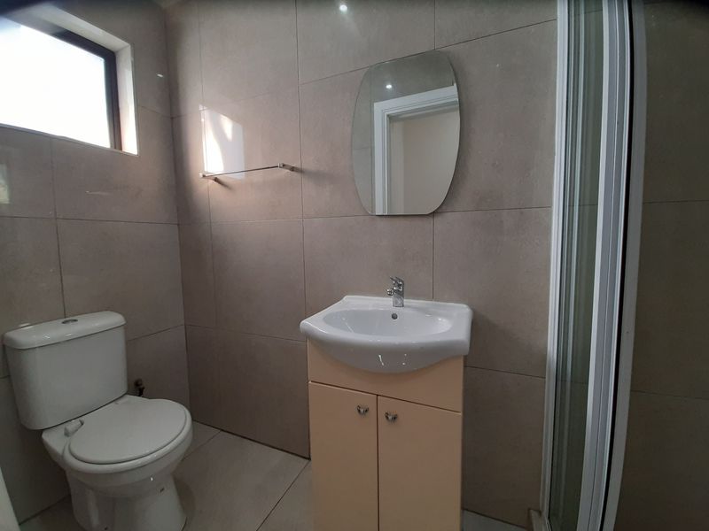 A clean, modern bathroom featuring a vanity cabinet with basin, a toilet, and a glass-enclosed shower with neutral wall and floor tiling.